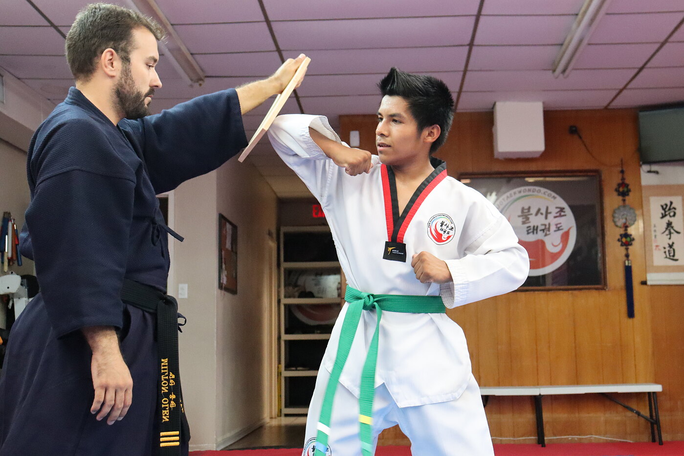 A student set to strike a board the instructor is holding up at head height