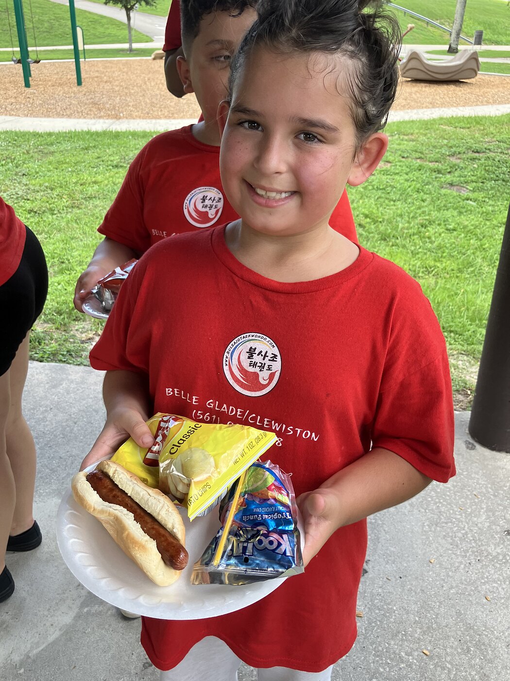 A camper in a Bulsajo camp shirt holding her lunch plate on a field trip day