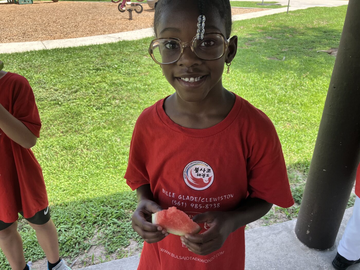 A camper in a Bulsajo camp shirt with a slice of watermelon at the park
