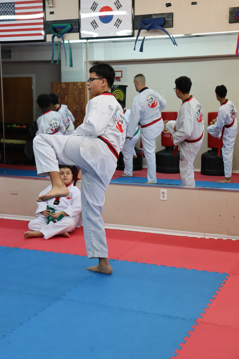 A student holding a kick out in the air on the count, with the rest of the line doing the same behind him